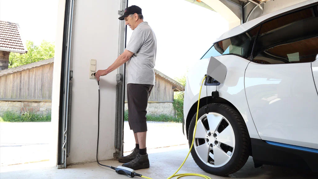 Charging Your EV. Man plugging in ev charger in his garage with a smart home charger