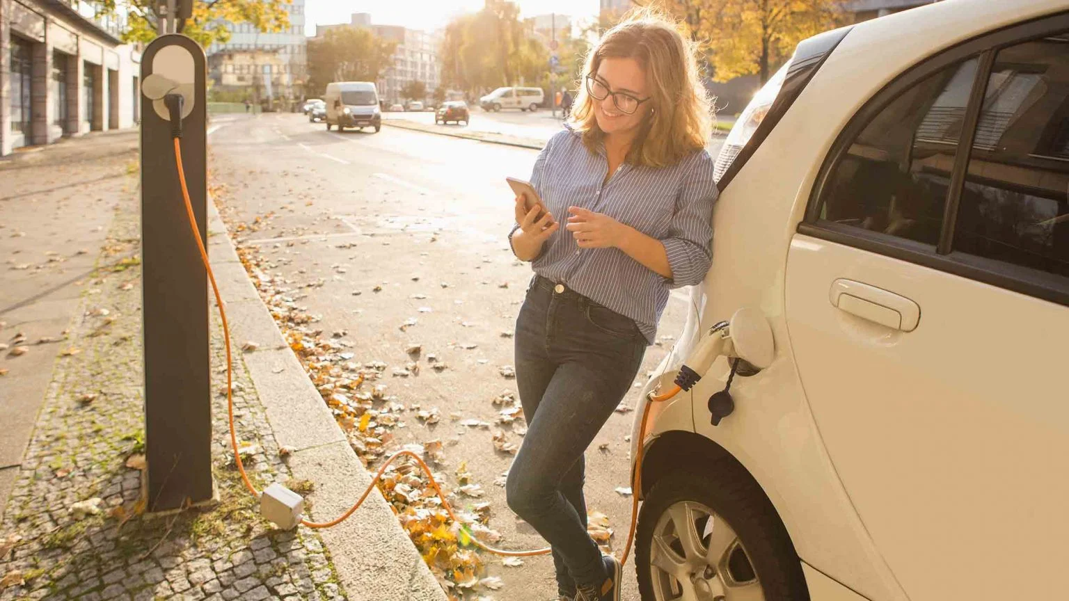 Person leaning against electric car looking at phone as the EV charges.economic and environmental benefits of an EV